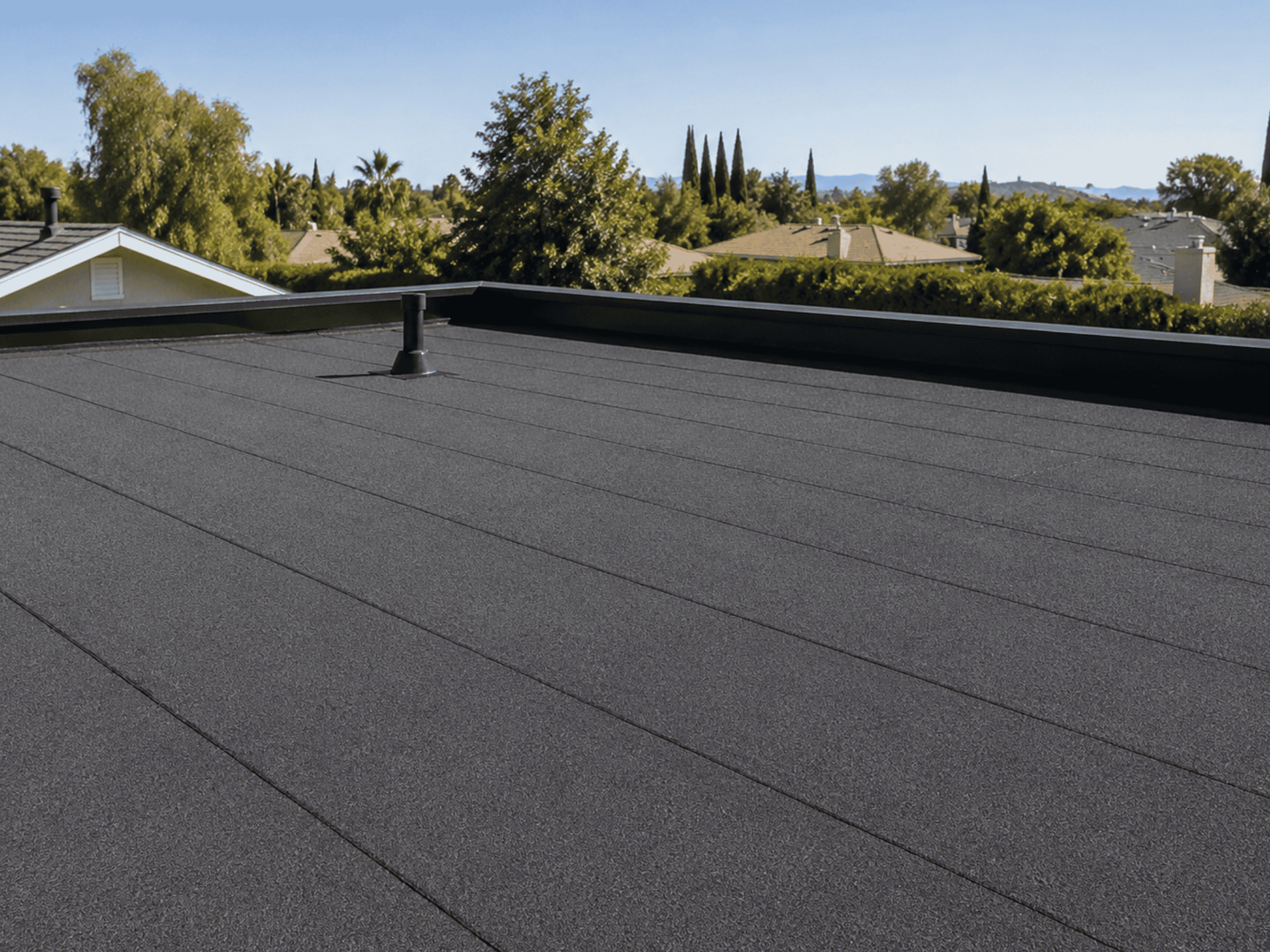 Finished gray granulated modified bitumen flat roof on a Southern California residential home with parapet edge and vent boot.