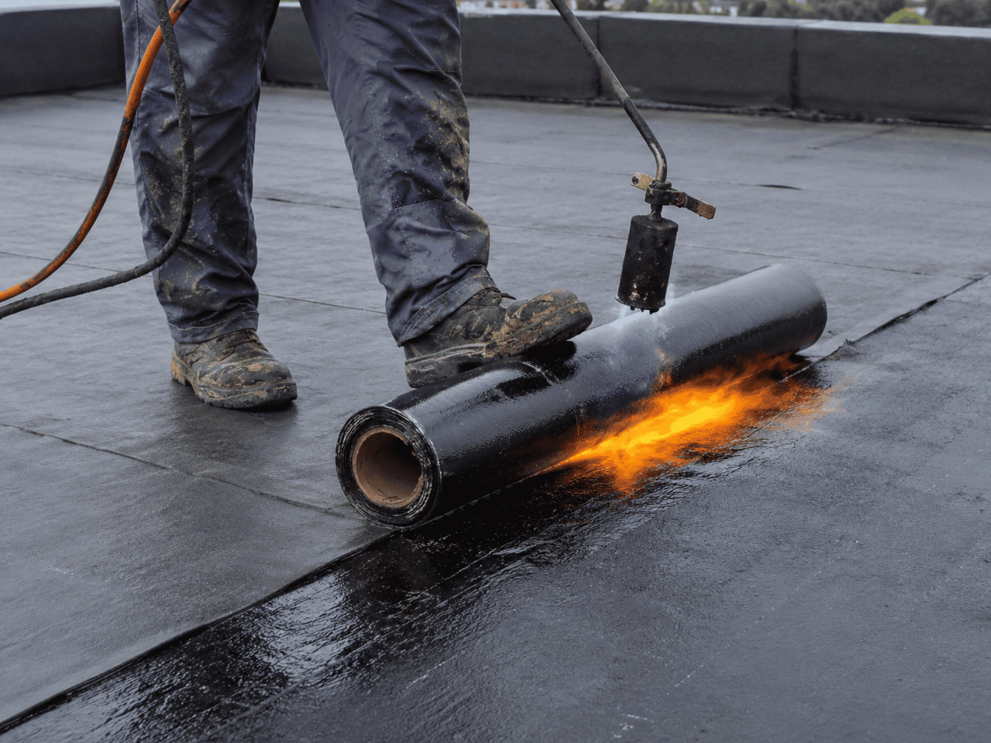 Roofing contractor torch-applying modified bitumen membrane during a flat roof installation.