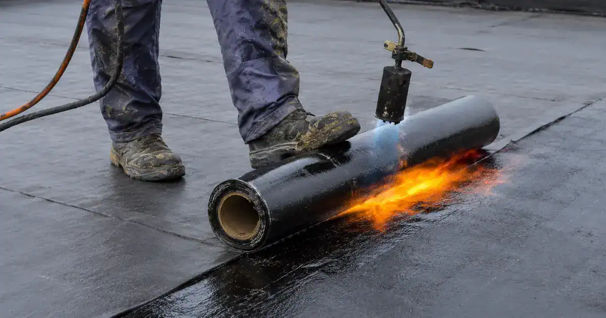 Roofing contractor torch-applying modified bitumen membrane during a flat roof installation.