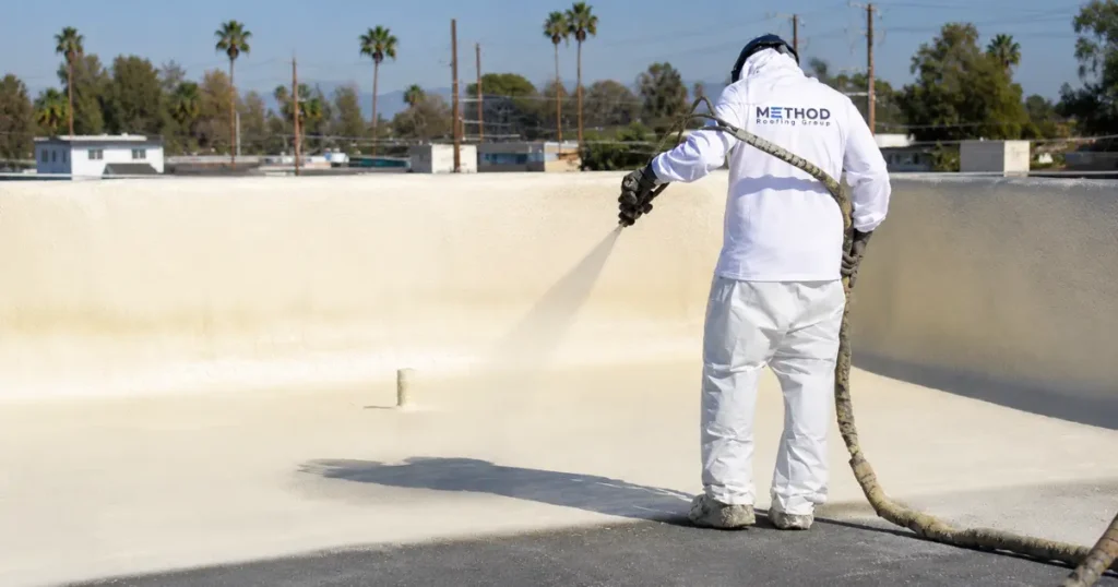 Method Roofing Group crew member applying spray polyurethane foam (SPF) on a commercial roof in Southern California using two-component spray equipment